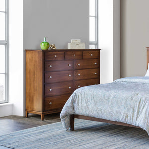 Eleven-drawer lady's dresser in warm brown wood staged in a bright bedroom beside a bed with paisley bedding