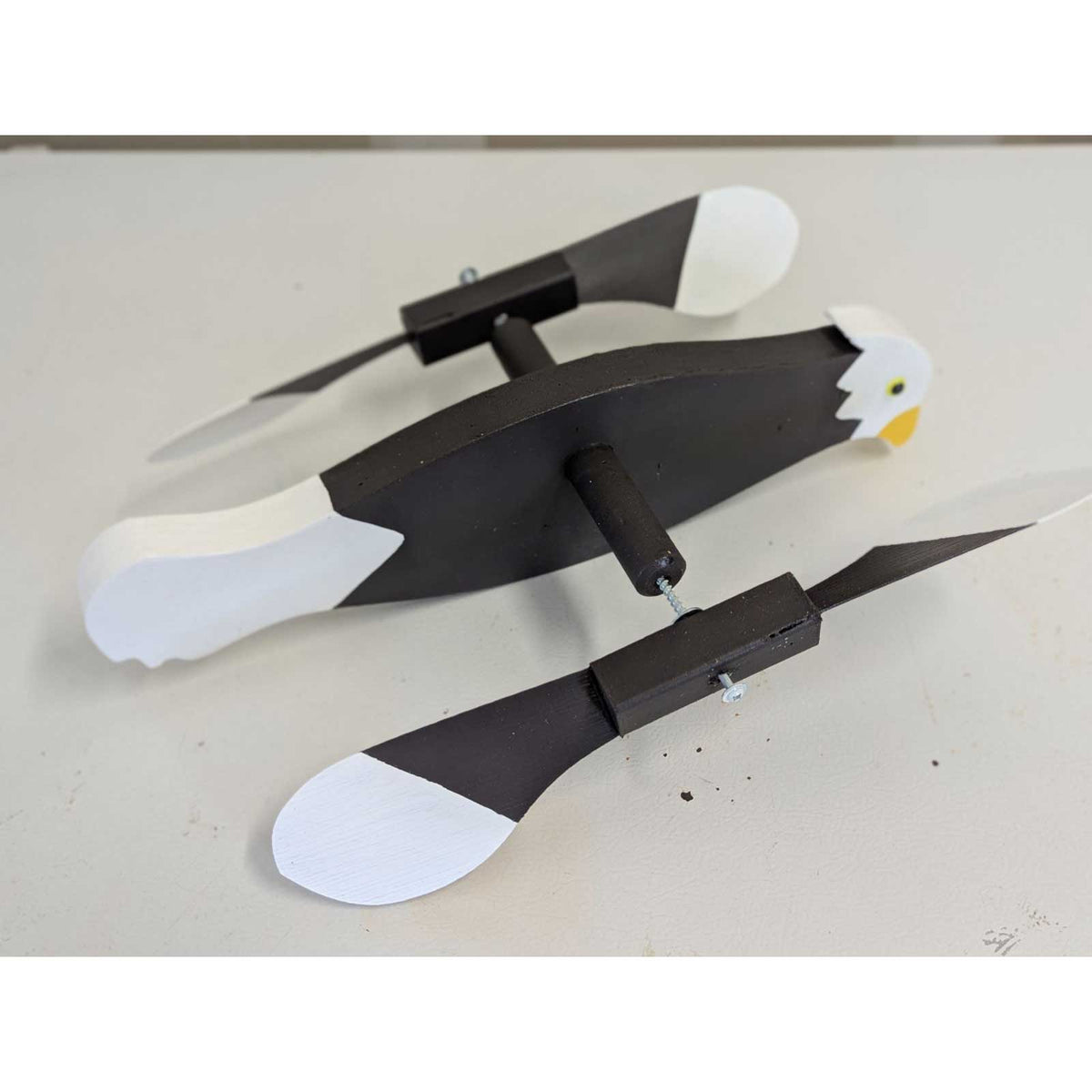 Bald eagle whirlybird with brown body and white paddle wing tips shown disassembled on a workbench with the wing rods