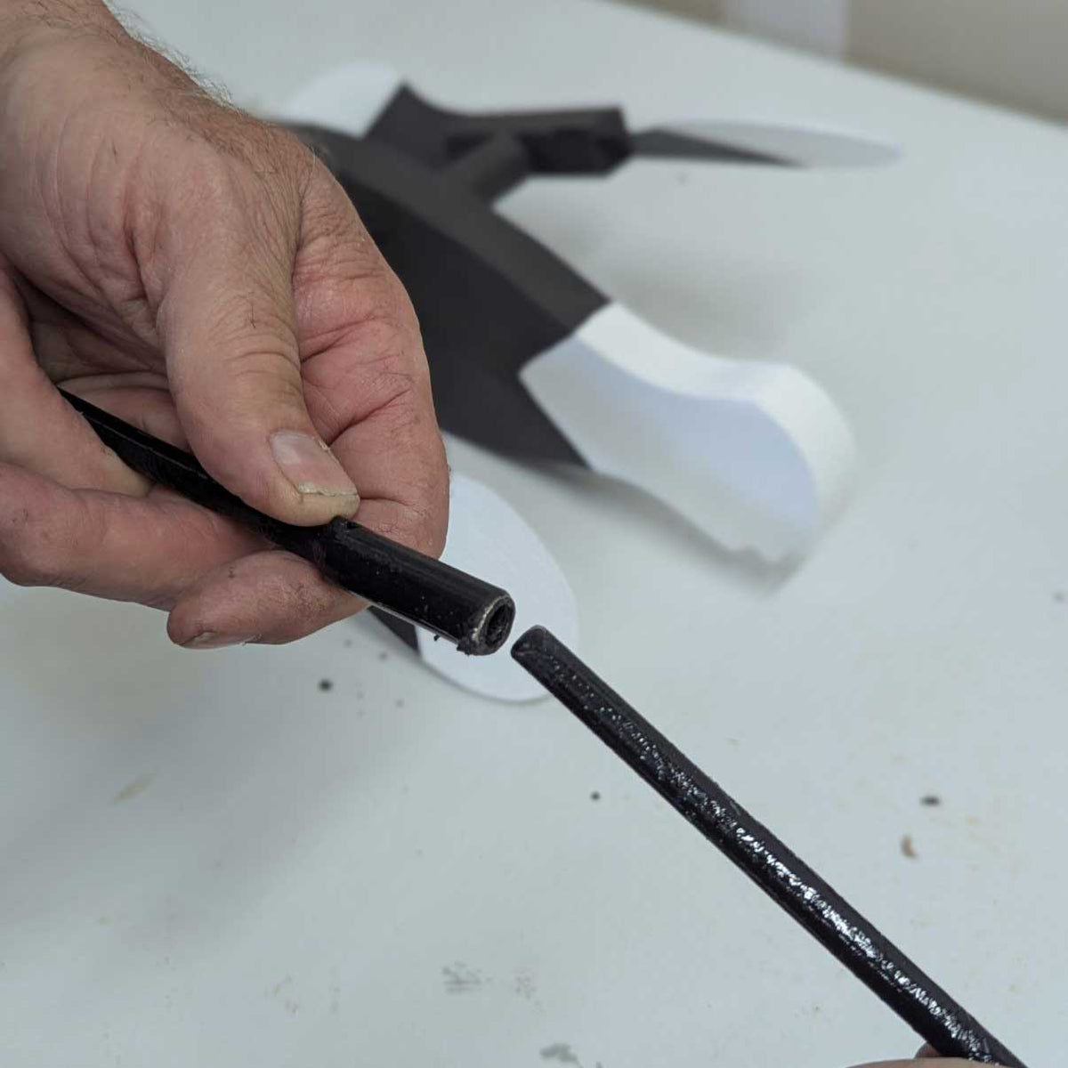 Close-up of hands holding the black metal rod and sleeve used to attach replacement whirlybird wings to the spinner body