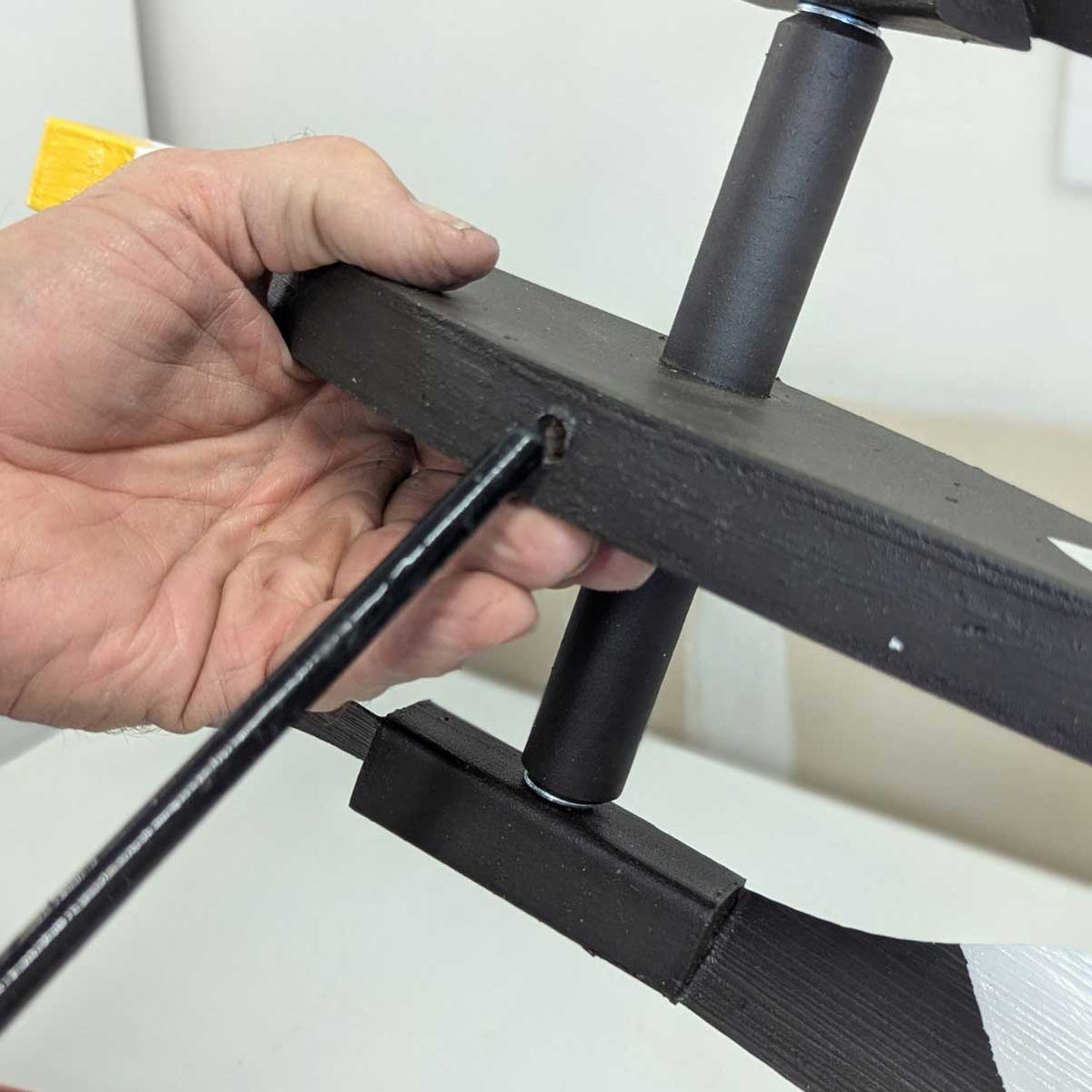 Hand holding a black metal bracket against a white background