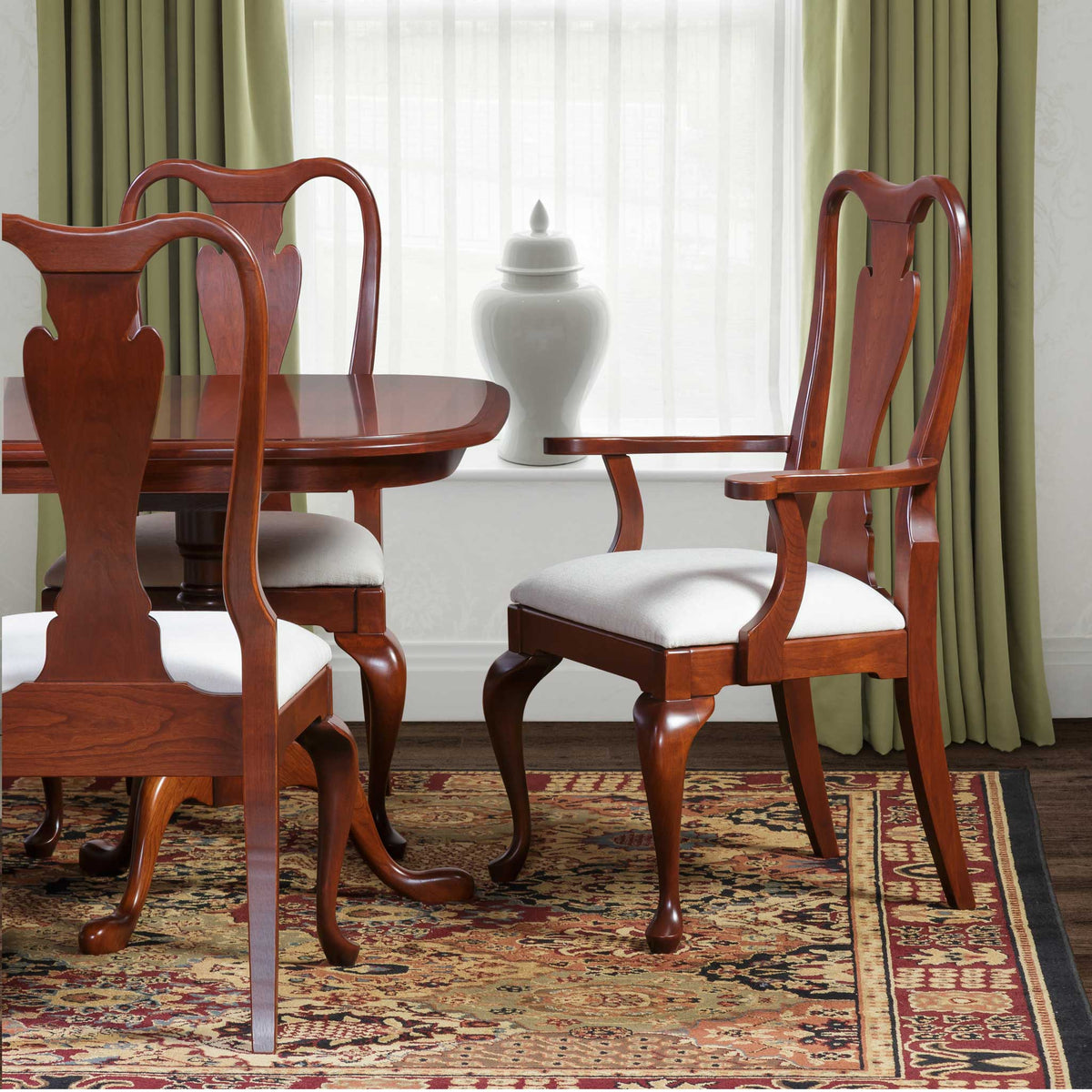 Cherry Queen Anne dining chairs with urn splat backs, ivory upholstered seats and cabriole legs on an oriental rug
