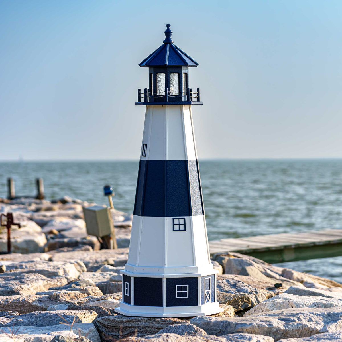 Navy and white lighthouse with blue lantern room on a stone jetty overlooking open water on a clear day
