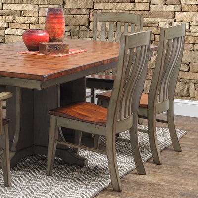 Sage green painted slat back dining chairs with stained wood seats around a two-tone pedestal dining table