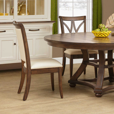 Upholstered dining side chair in oak with cream fabric seat and padded back beside a round table and white hutch
