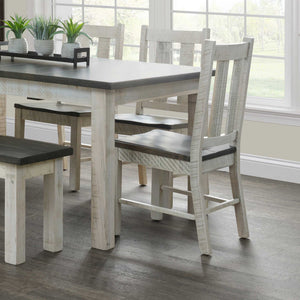 Distressed white slat-back dining chairs with gray wood seats tucked under the rustic two-tone Alamo dining table