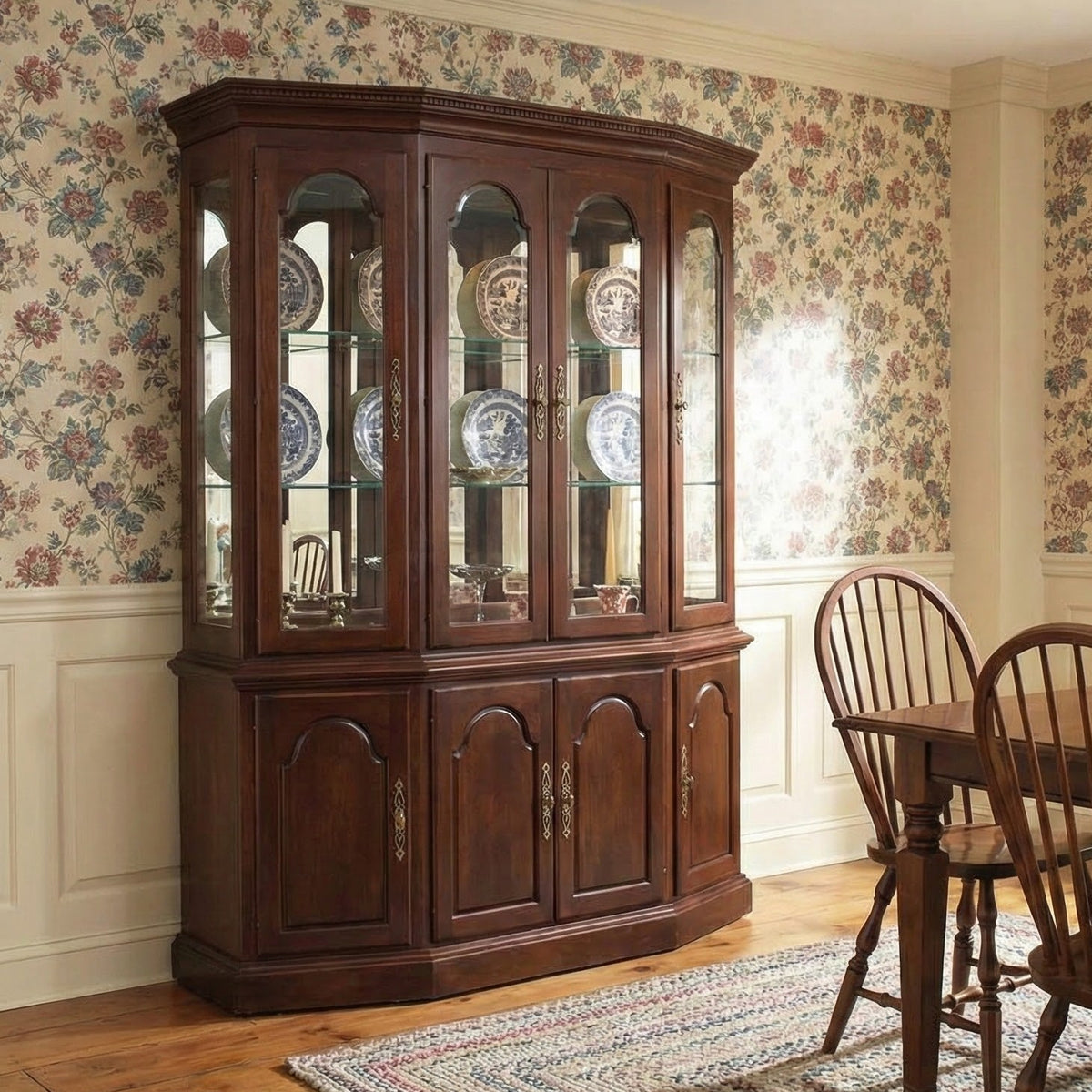 Dining room with wooden china cabinet and table set against floral wallpaper.