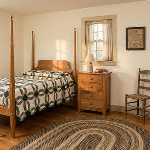 Cherry four drawer bedside chest beside a pencil post bed with wedding ring quilt in a colonial room