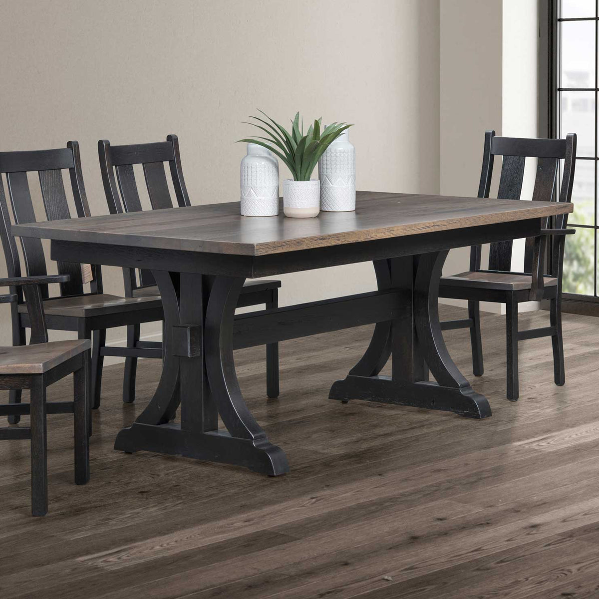 Two-tone dining table with gray plank top and black trestle base, styled with white vases and paired black chairs