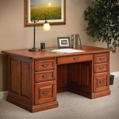Cherry executive desk with lamp and books, framed sunrise painting above and a ficus tree beside it