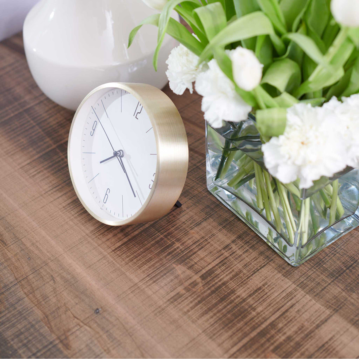 Reclaimed wood dresser top styled with a brushed gold clock, white tulips and carnations in a glass vase
