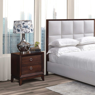 Two drawer nightstand in dark cherry with silver ring pulls, beside a gray upholstered panel bed and city window