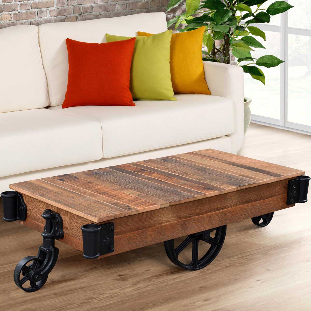 Industrial reclaimed wood factory cart coffee table with black cast iron wheels styled in front of a white sofa with colorful pillows