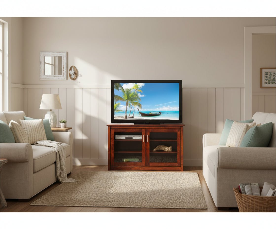 Cherry two door LCD TV stand with glass fronts and interior shelves, set against a paneled wall between two cream sofas