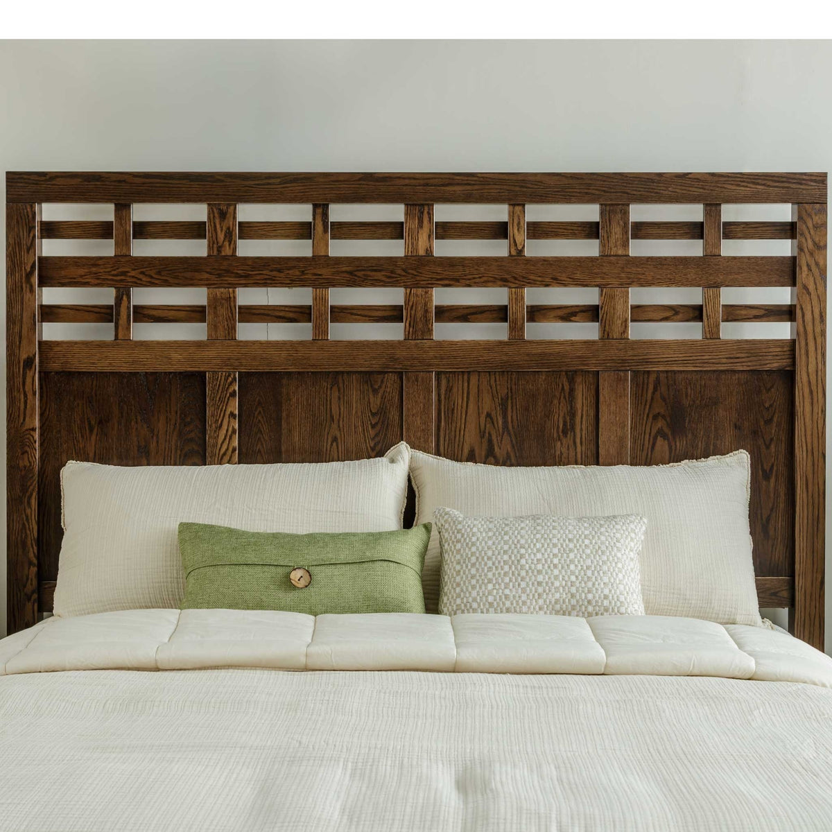Dark oak lattice headboard behind cream pillows and a green accent pillow on a bed dressed in white bedding