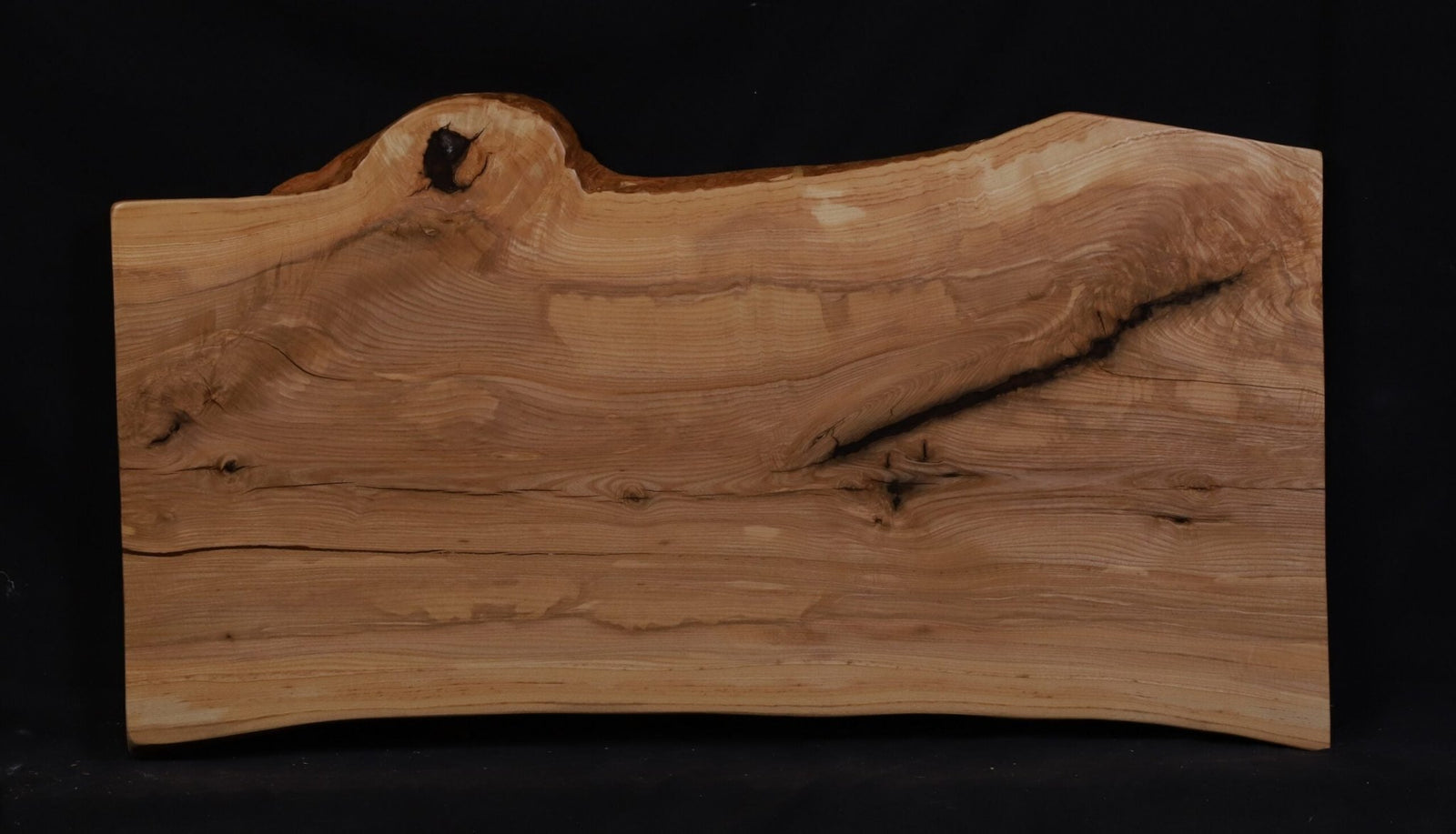 Rectangular ash live edge coffee table slab with wavy bark edges, a dark knot and rippling grain on black