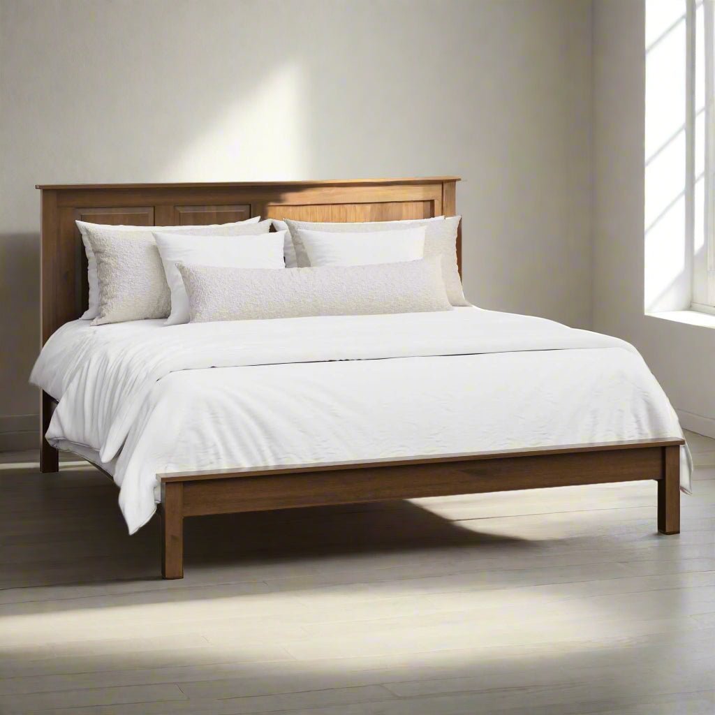 A king-sized solid wood high panel bed frame with a low footboard, shown in a brown stain finish, made with pillows and a bedsheet.