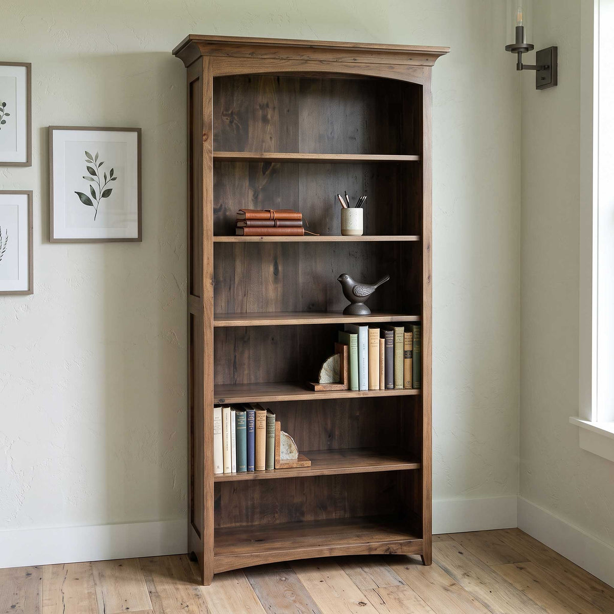 A tall, rustic wooden bookcase with five shelves stands against a light beige wall in a room with hardwood floors. The bookcase is styled with books, a small bird figurine, and a cup on the shelves.