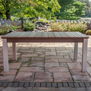 Rectangular poly patio dining table with weathered gray plank top and white legs on a stone patio by a waterfall garden