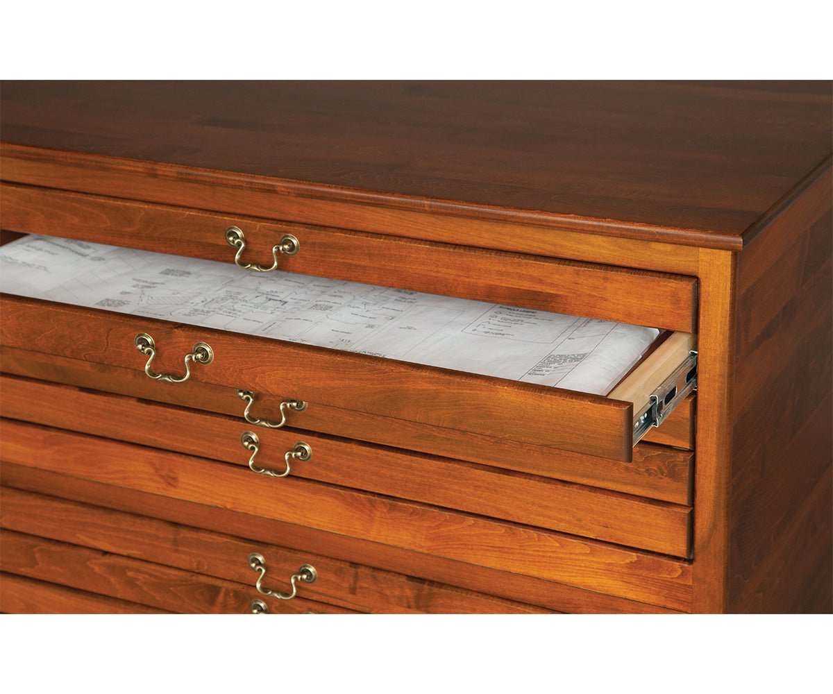 Flat file cabinet drawer slid open with rolled blueprints resting inside, showing brass bail pulls on cherry drawer fronts
