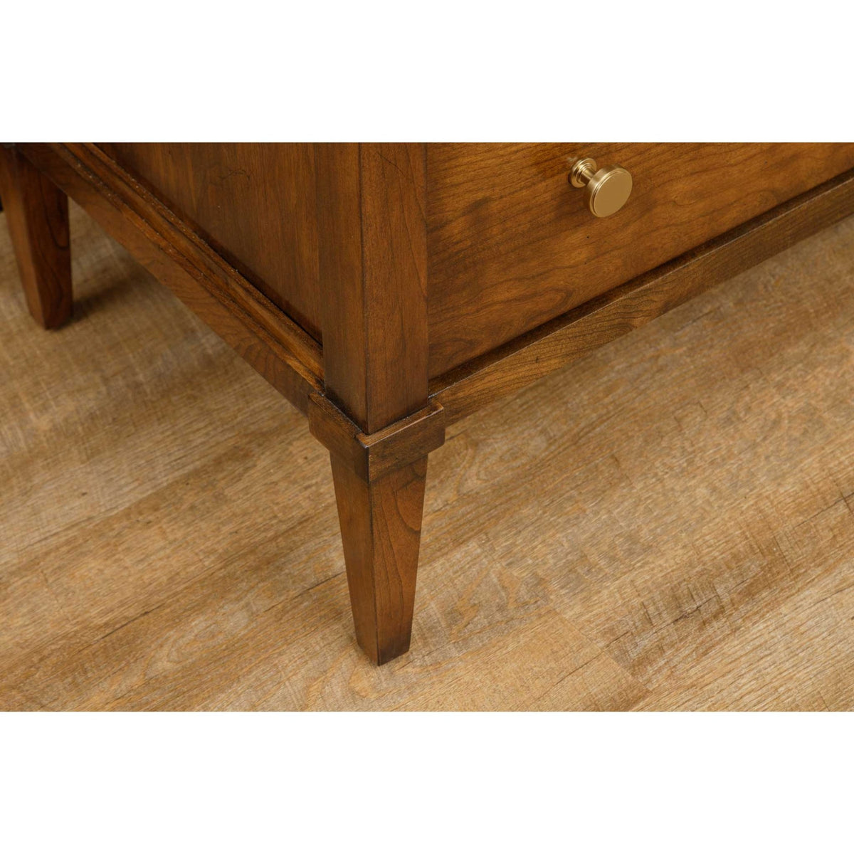 Detail of a cherry nightstand base with a square tapered leg, molded skirt and round brass knob