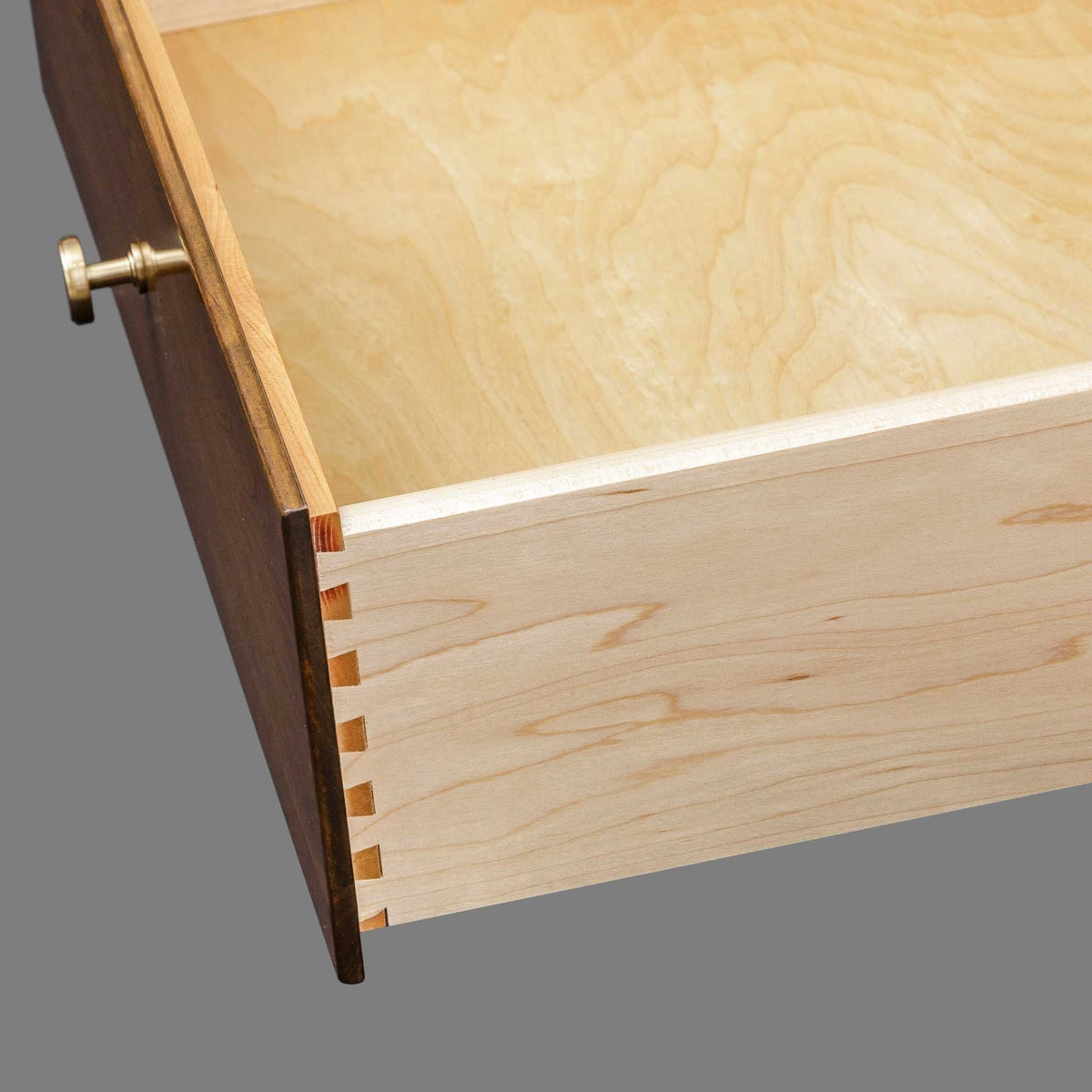 Dovetail joinery view of the nightstand drawer, maple box with cherry front and brass knob on gray