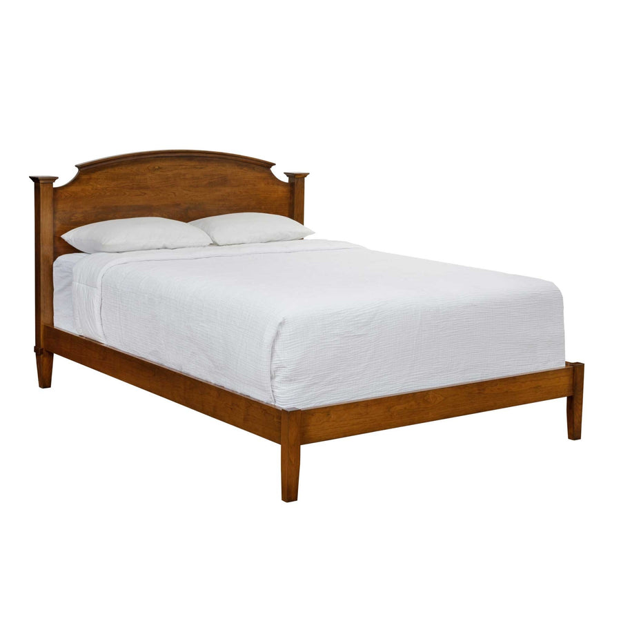 Cherry bed with an arched headboard and low footboard rail on tapered legs, white bedding on a white background