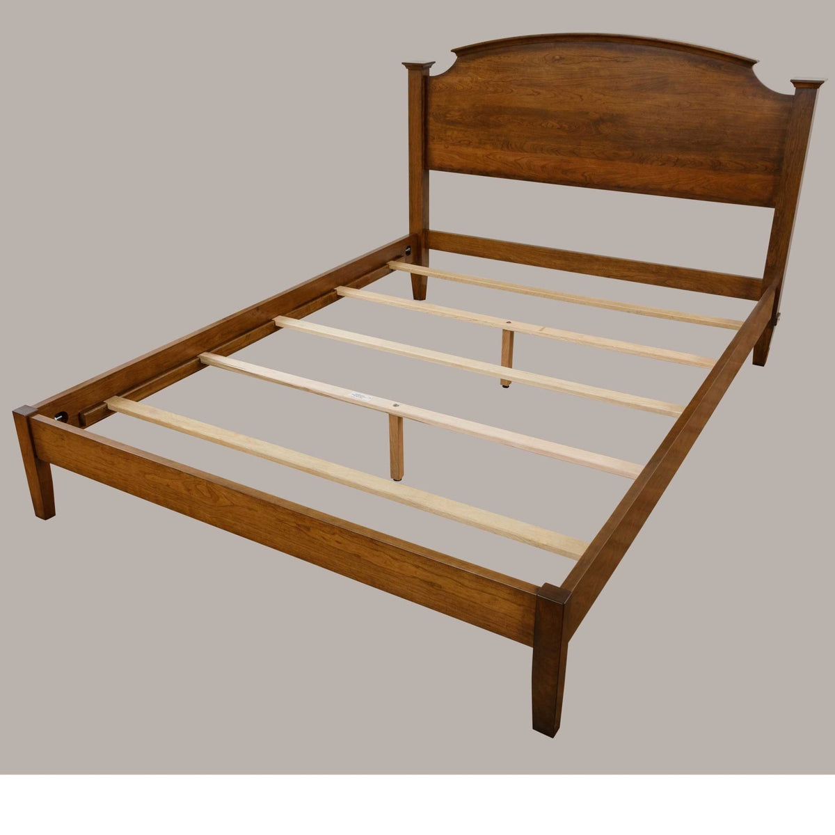 Cherry bed frame with arched headboard and low side rails shown unmade with pale maple support slats
