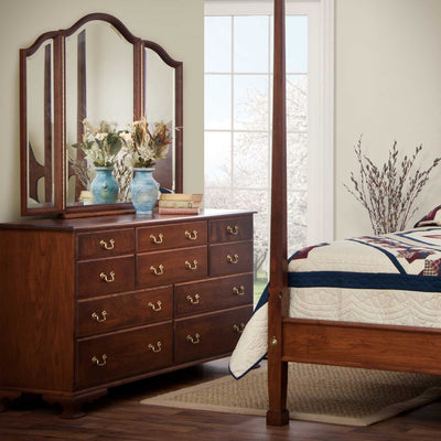 Cherry triple dresser with ten drawers and brass pulls, topped by an arched triview mirror and blue vases