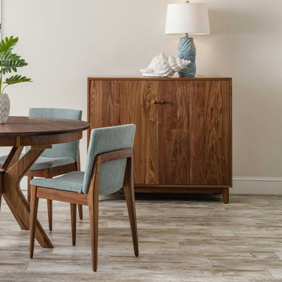 Walnut mid century server cabinet with two flat panel doors beside a dining table and green chairs