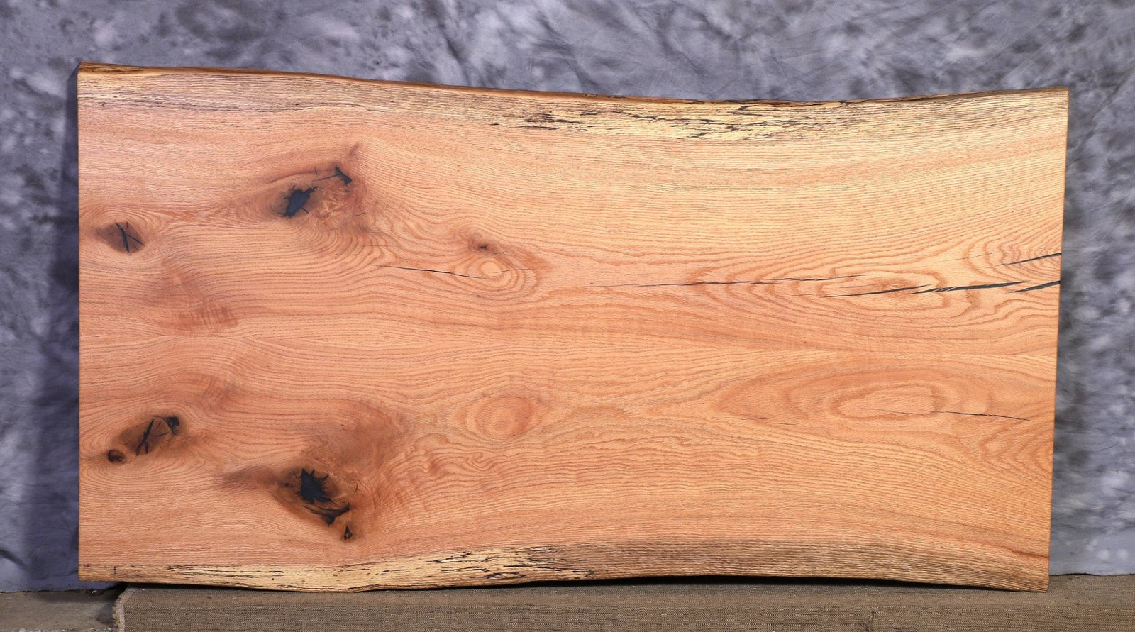 Book matched oak live edge slab with knots, dark inclusions and mirrored grain on a gray backdrop