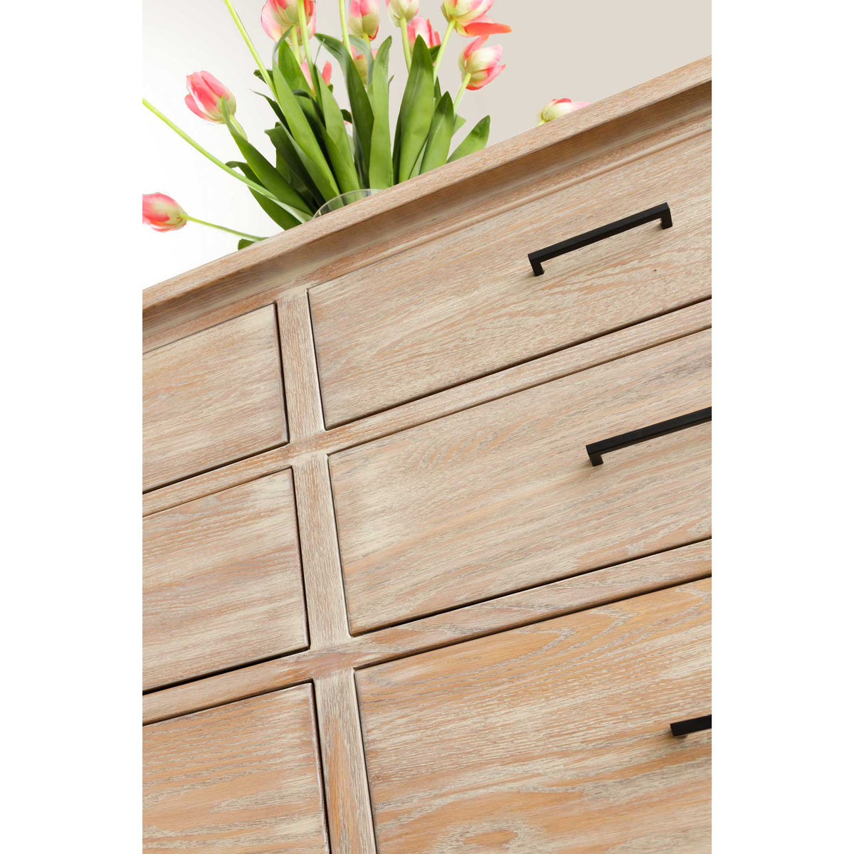 Close-up of the whitewashed dresser's beveled top and drawer fronts with slim black bar pulls and tulips