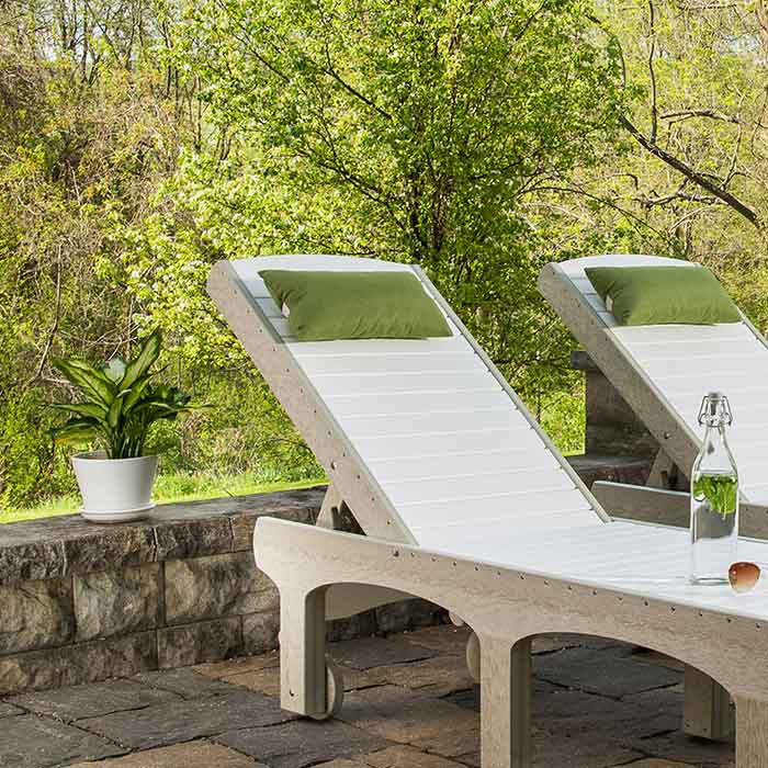 Green rectangular pillows resting on white and tan poly chaise lounges on a stone patio