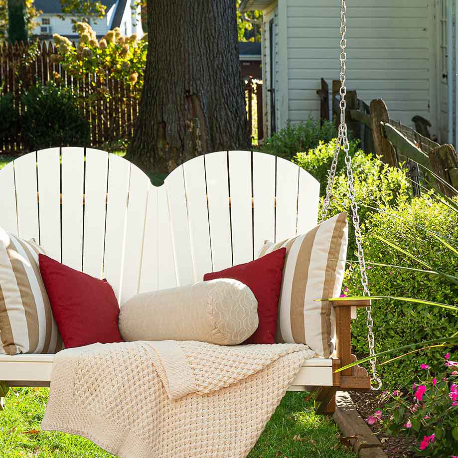 Cream cylinder bolster among striped and red pillows on a white fan back porch swing in a garden