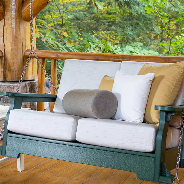 Taupe cylinder bolster pillow with white and gold cushions on a green poly porch swing at a log cabin