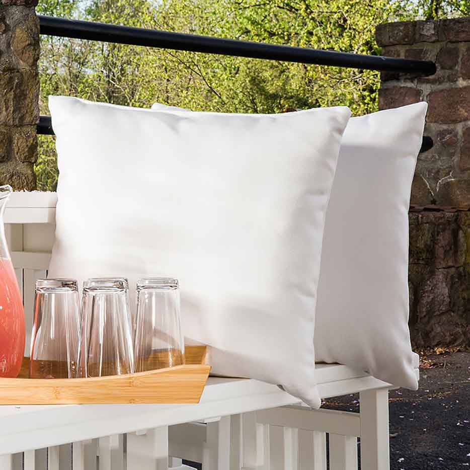 Pair of white solid Sunbrella square pillows on a white poly bench beside a pitcher and glasses on a bamboo tray