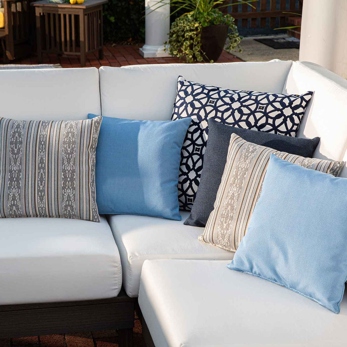 Assorted Sunbrella outdoor pillows in blue, gray, tan stripe and navy medallion print on a white patio sectional