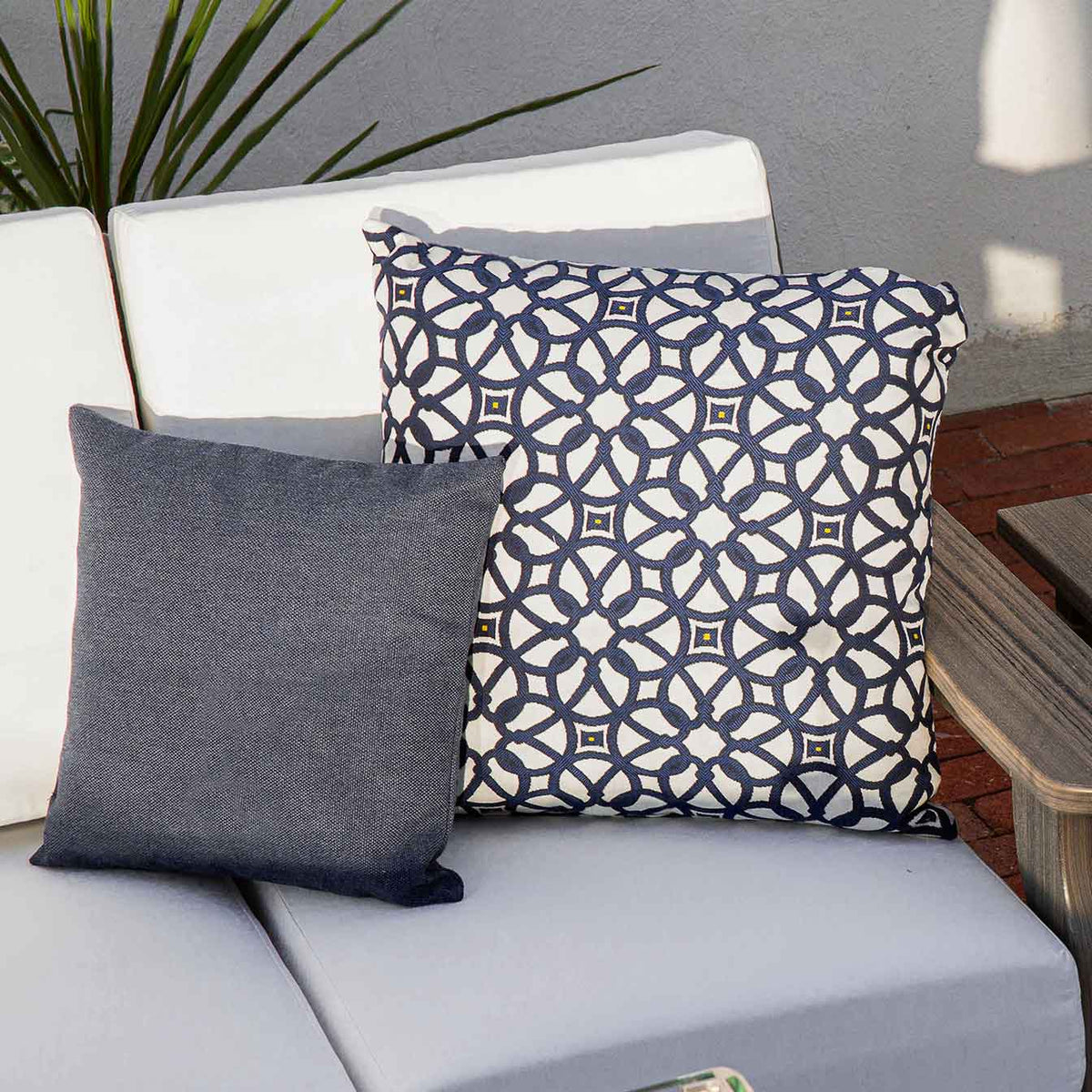 Navy medallion lattice pillow and a solid denim blue pillow arranged on a white cushioned outdoor sectional seat