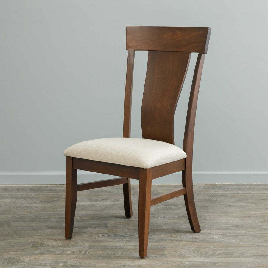 Walnut toned dining chair with a curved hourglass back panel and cream linen upholstered seat, standing on gray wood flooring