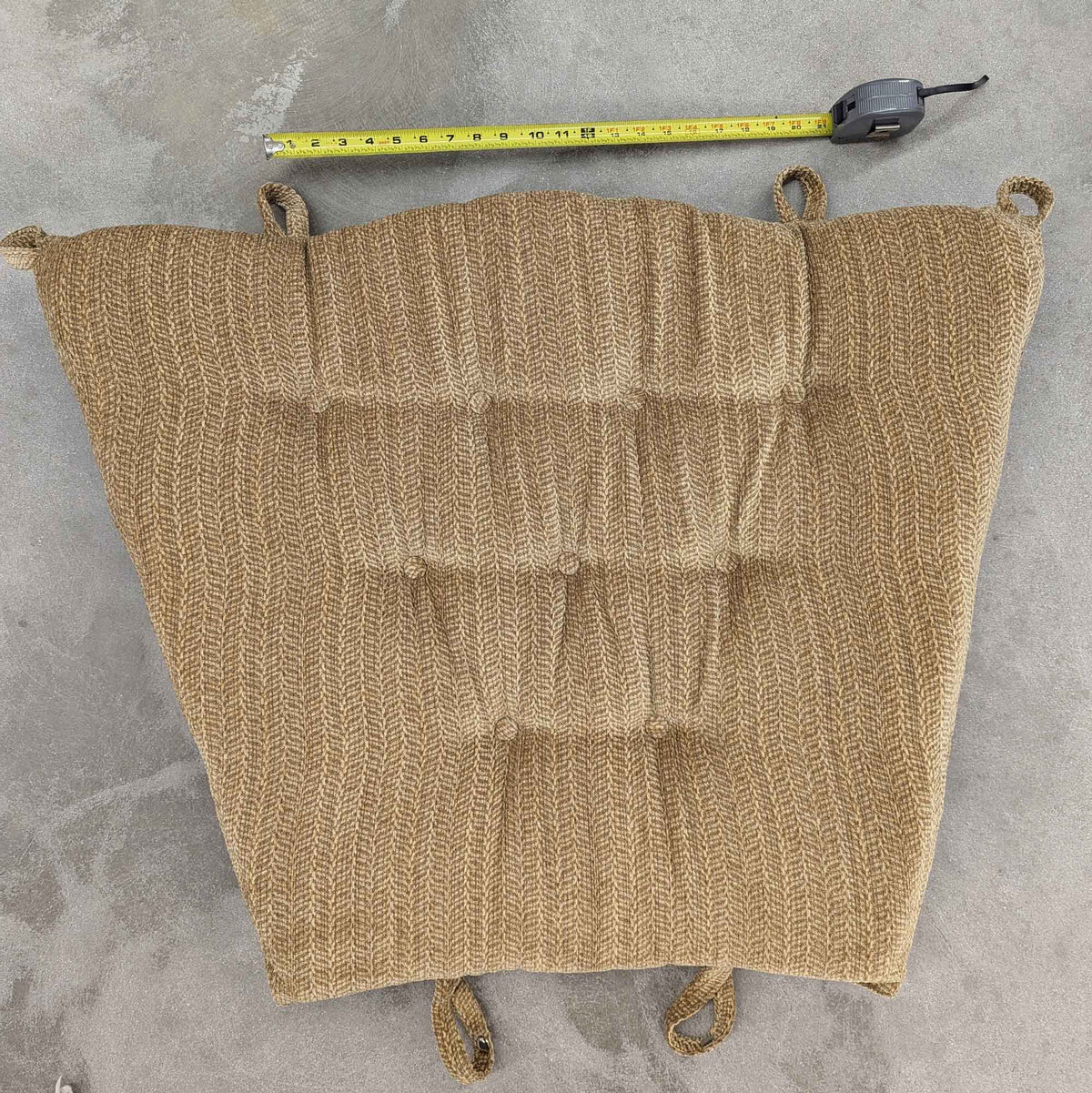 Replacement glider back cushion in tan woven fabric with corner ties, measured against a tape on the floor