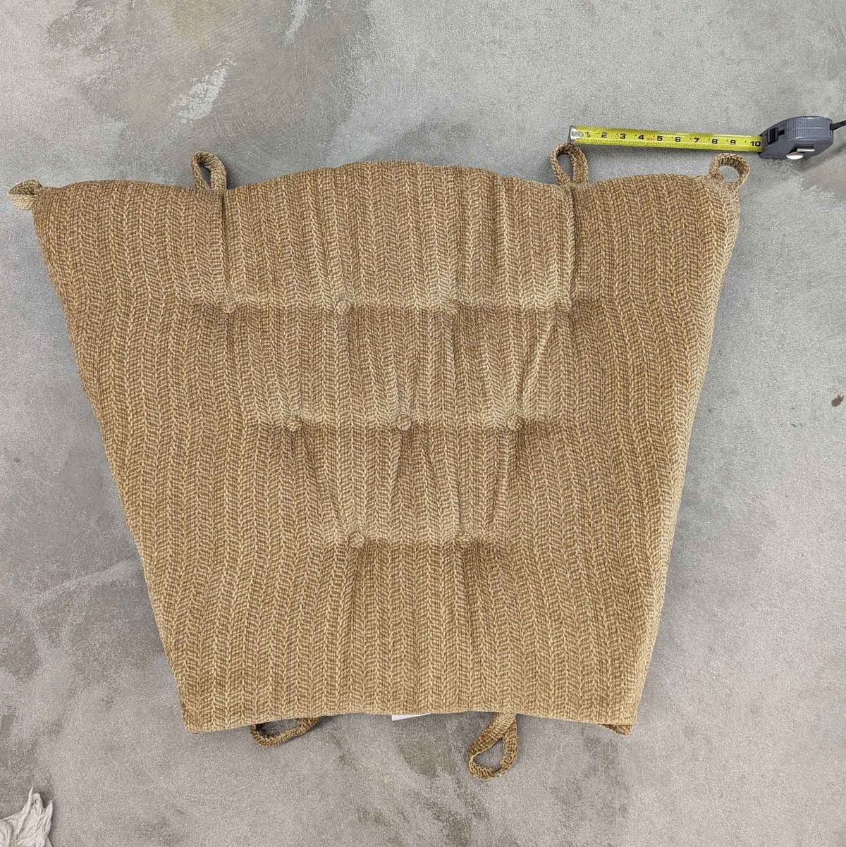 Tan chevron patterned glider back cushion laid flat on concrete with a tape measure showing its width