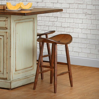 Two walnut toned saddle seat bar stools with turned splayed legs at a sage green kitchen island by a white brick wall