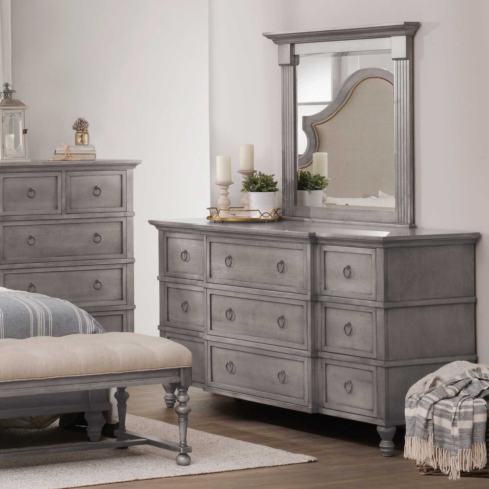 Gray nine-drawer dresser with framed mirror styled with candles beside a tall chest and upholstered bench