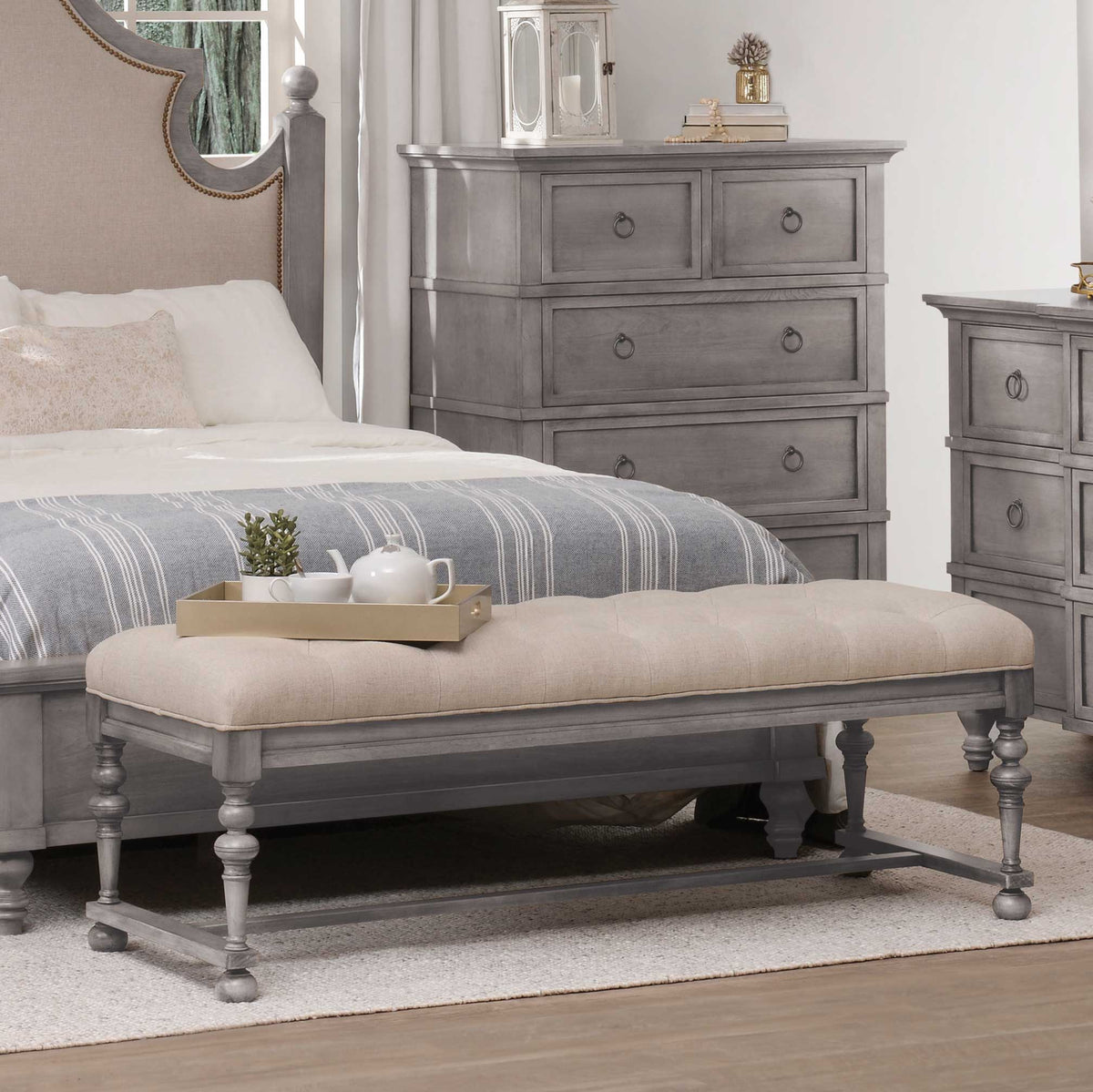 Gray tufted linen bedroom bench with turned legs and stretcher base placed at the foot of an upholstered bed
