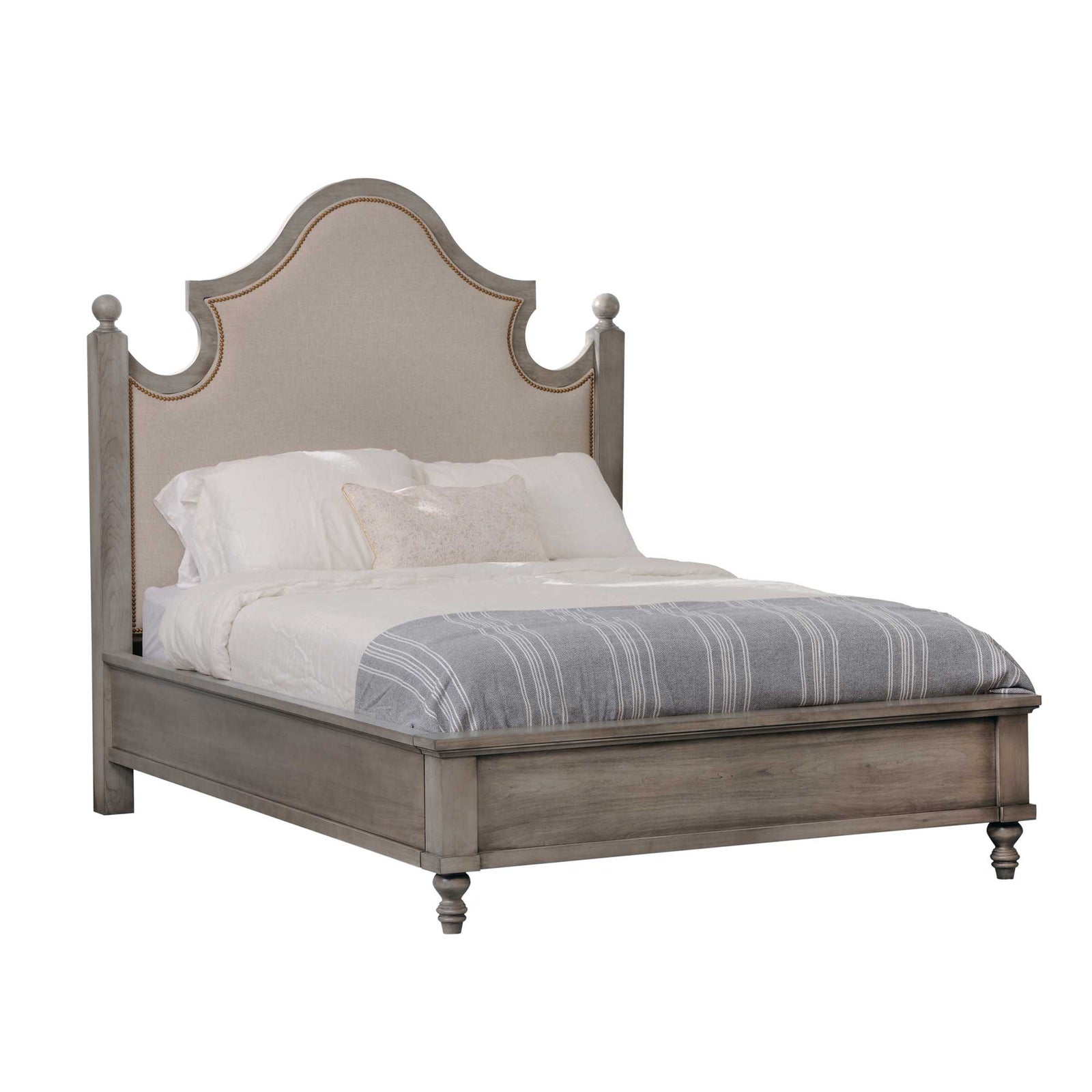 Gray upholstered bed with arched linen nailhead headboard, ball finials and tufted bench in a sunlit bedroom