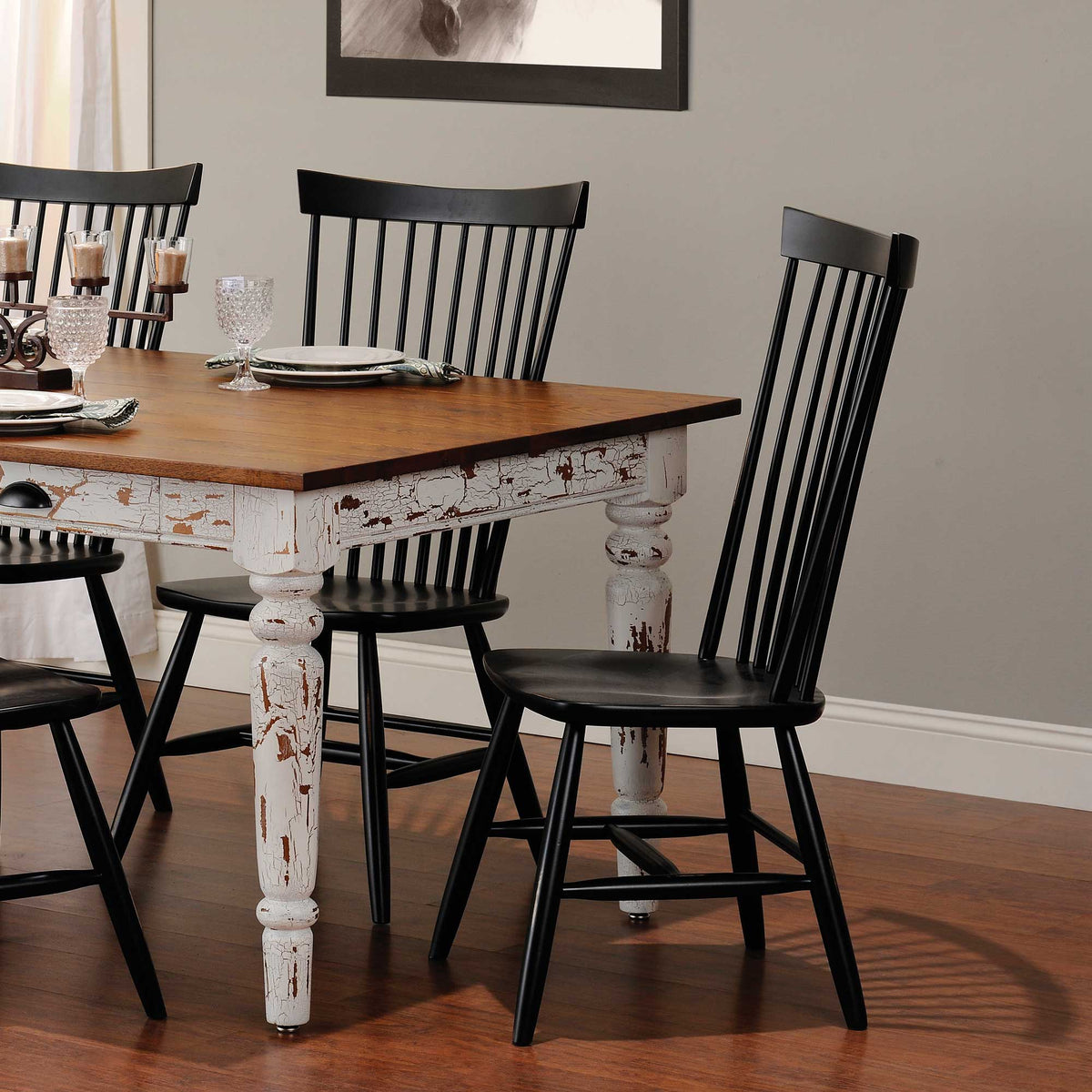 Distressed white farmhouse table with a plank top and black spindle back chairs set with glassware