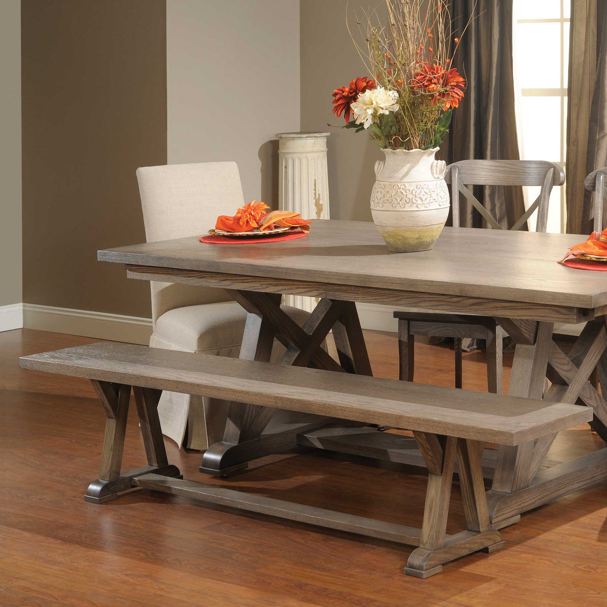 Weathered gray trestle dining bench with a thick plank seat pulled up to a matching X-base table