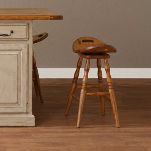 Swivel saddle bar stool in golden oak with a hand hold cutout seat and turned legs beside a cream painted kitchen island