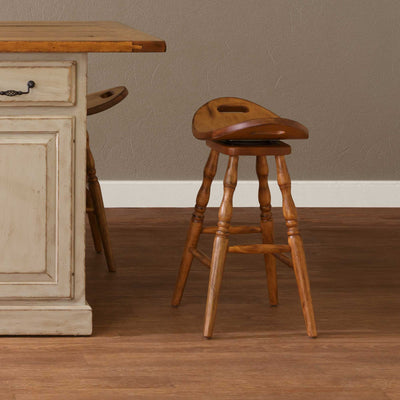 Swivel saddle bar stool in golden oak with a hand hold cutout seat and turned legs beside a cream painted kitchen island