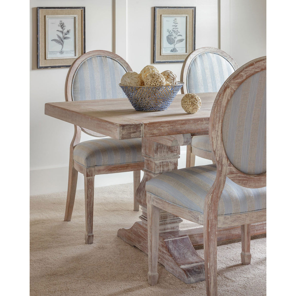 Whitewashed trestle table with a plank top paired with light blue striped oval back chairs and a wire bowl
