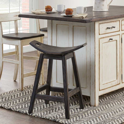 Dark gray swivel saddle stool with a curved backless seat and hand hold cutout at a distressed white kitchen island